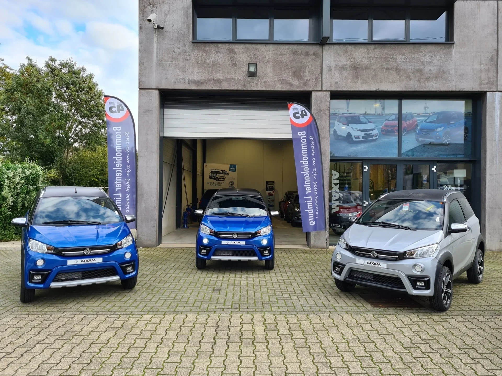 BrommobielCenter Limburg Filiale Beek – drei Mopedautos vor dem Gebäude mit Ausstellung und Werbebannern